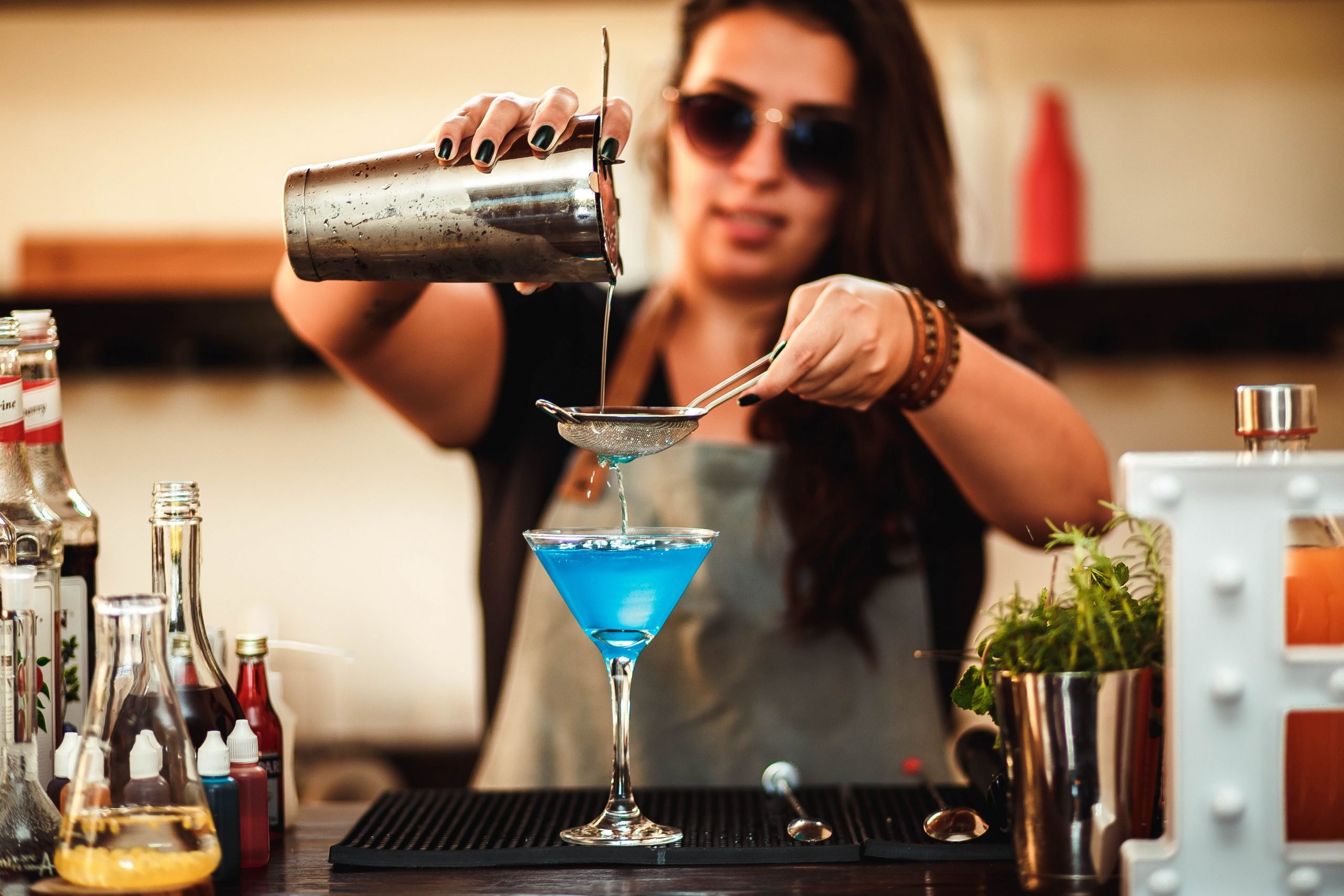 A photo of a bartender pouring a cocktail in a martini glass