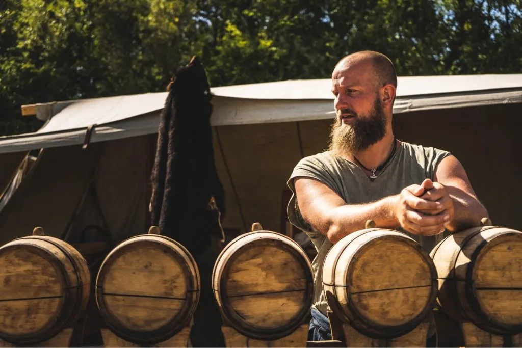 A photo of a man leaning on whiskey barrels.
