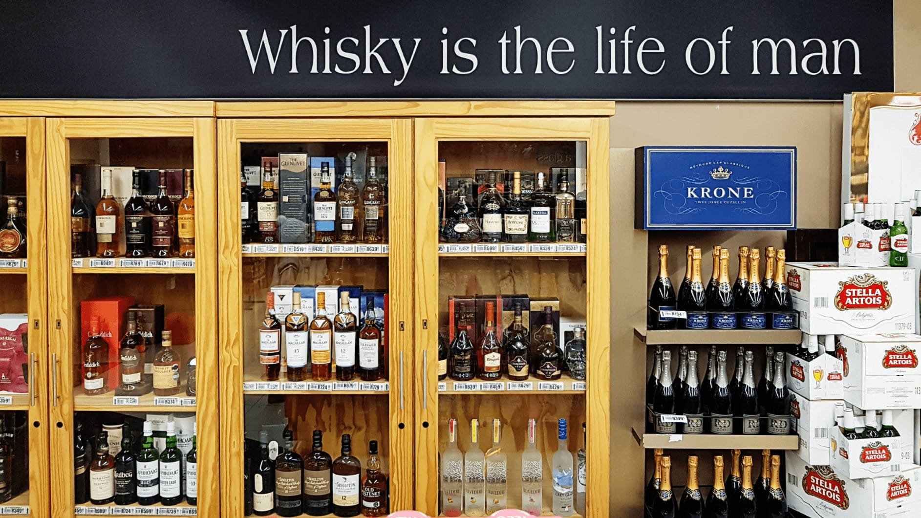 A photo with whiskey bottles on shelves and a sign that says "Whisky is the life of man"