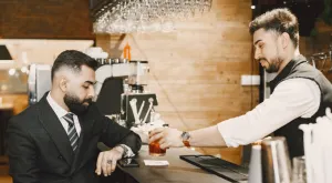 male alcohol field sales rep in suit sitting at bar being served cocktail by male bartender