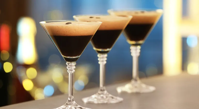 three espresso martinis made at home, black liquid with tan frothy topping and coffee beans for garnish in martini glasses